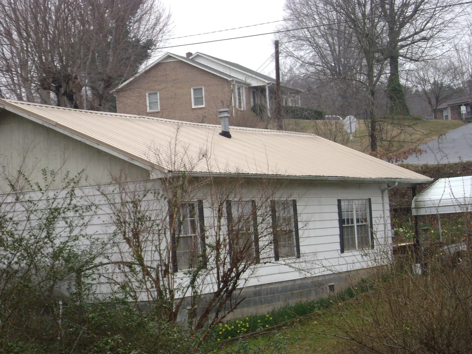 Tan metal roof on a white sided house set into a hillside — Commercial Roofing by Roofing Brothers in Julian